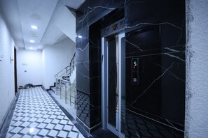 A hallway with a tiled floor, a staircase, and an elevator with a digital display. - Forest view 1BHK Premium studio appartment (New Delhi)