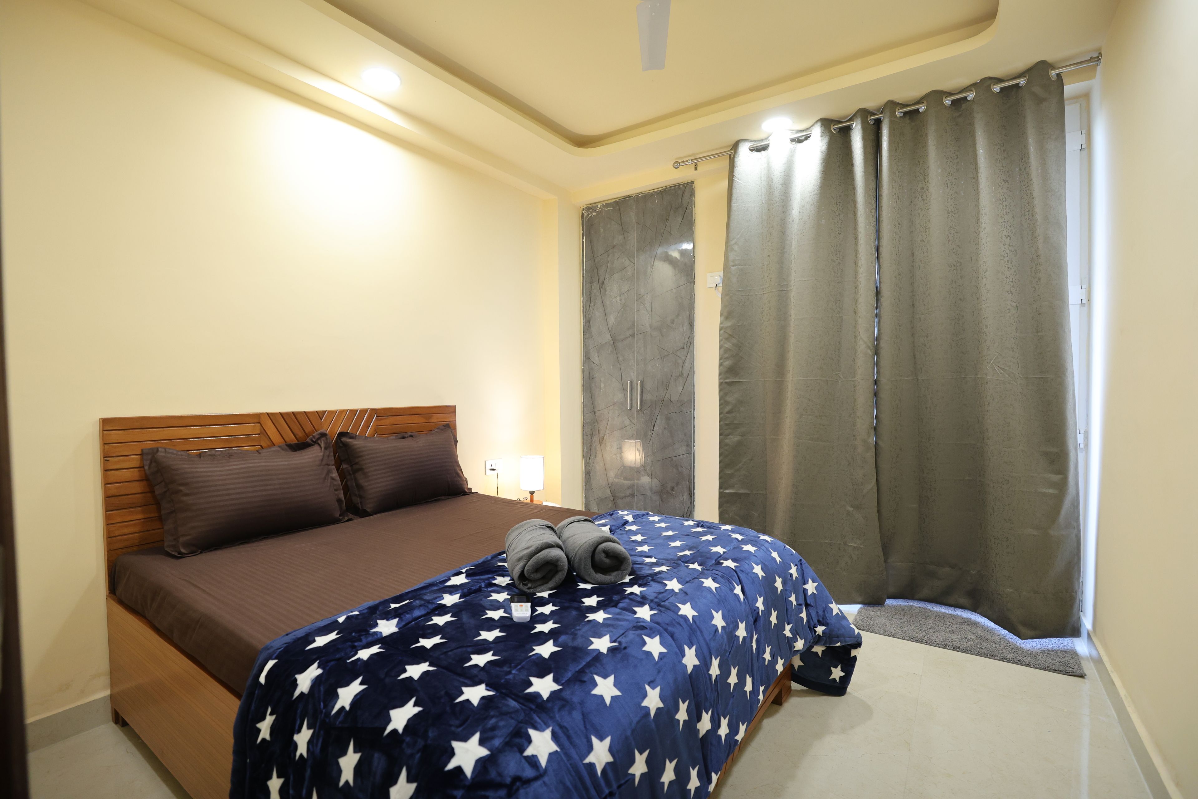 Un dormitorio con cama, mesita de noche, lámpara, ventana con cortinas y cabecero de madera.