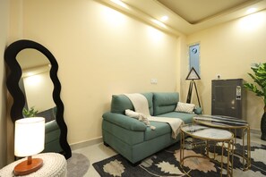A living room with a sofa, a round coffee table, a lamp, a mirror, a clock, and a potted plant. - Forest view 1BHK Premium studio appartment (New Delhi)