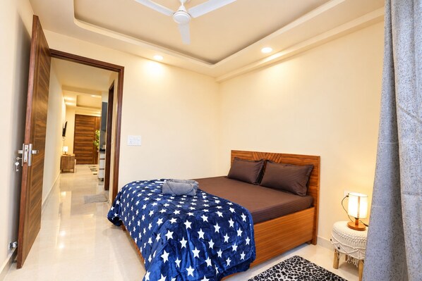 A bedroom with a bed, a nightstand, a lamp, and a ceiling fan. - Forest view 1BHK Premium studio appartment (New Delhi)