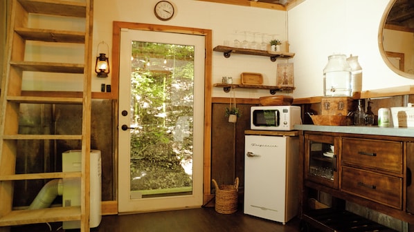 A compact kitchen with a refrigerator, microwave, and wooden shelves.