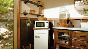 Een kleine keuken met een witte koelkast, een magnetron en een houten kast met glazen deuren.