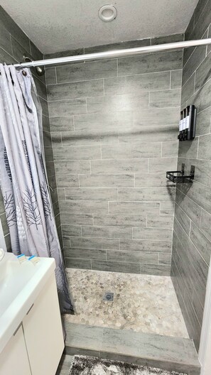 Eine Dusche mit grauen Fliesen, eine weiße Badewanne und ein Duschvorhang mit Blätermotiv.