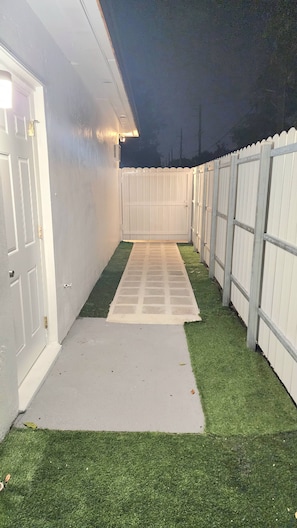 A narrow pathway leading to a gated area with artificial grass and a white fence. - Private King Studio near Beach, FLL & Hard Rock (Hollywood)