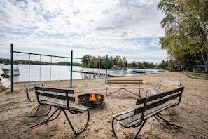 A beach with a fire pit and benches, overlooking a lake with boats. - Cozy Corner at Sommer Dorf (West Branch)