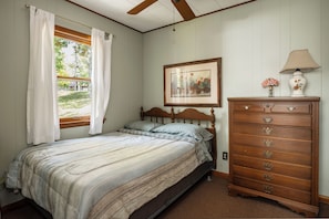 A bedroom with a bed, a dresser, a ceiling fan, a window with curtains, and a framed picture on the wall. - Cozy Corner at Sommer Dorf (West Branch)
