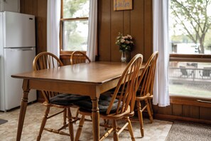 Una mesa de comedor de madera con cuatro sillas, un refrigerador y una ventana con vista a árboles.
