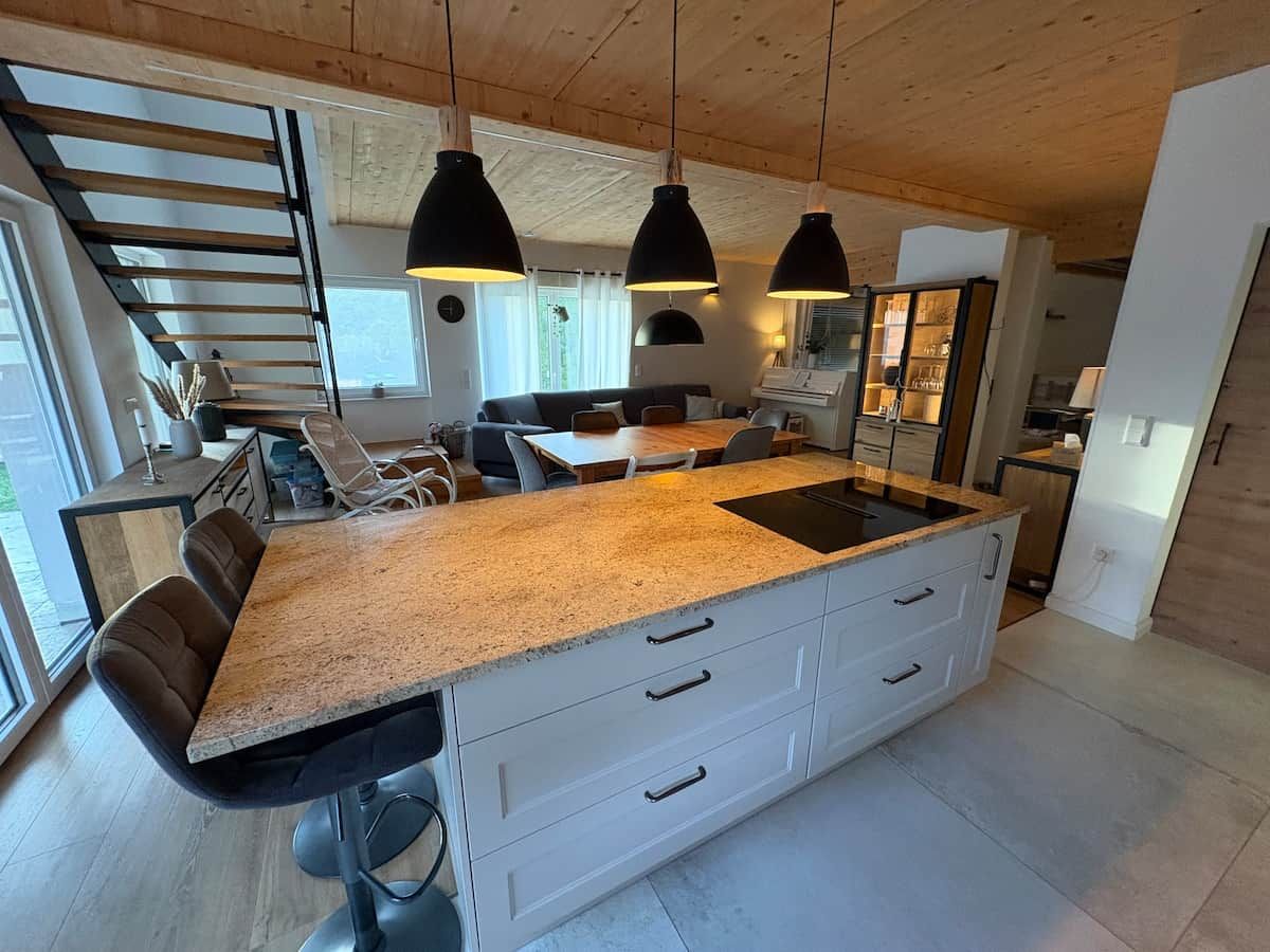 A modern kitchen with a central island, pendant lighting, and a staircase leading to an upper level.