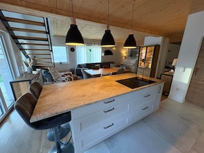 Een moderne keuken met een centraal eiland, hanglampen en een trap naar een hoger gelegen verdieping.