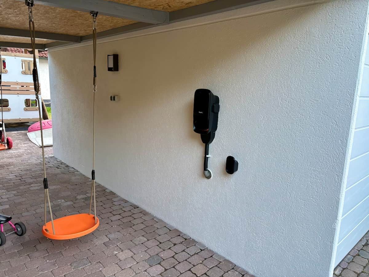 A covered outdoor area with a swing set and a wall-mounted device.
