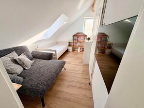 Een slaapkamer met vide, een schuine kap, een grijze bank, een houten vloer en een klein boekenrek.