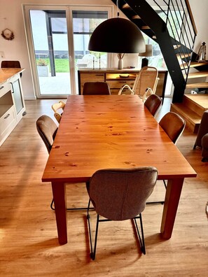 Un vaste espace dédié à la salle à manger, avec une longue table en bois et de nombreuses chaises, un escalier et une vue sur l’extérieur.