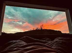 A window with a view of a sunset over a hill, with a blanket partially visible in the foreground. - Ferienhaus Traumzeit by Kringe (Vöhl)