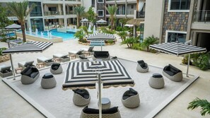 A poolside area with lounge chairs, umbrellas, and a central water feature. - 1BR Retreat | Pool & Jacuzzi | Near Eagle Beach (Noord)