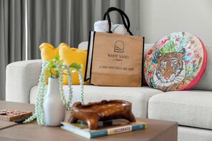 A living room with a sofa, a coffee table, a decorative bowl, a white vase with plants, a wooden sculpture, a book, a colorful embroidered pillow, and a brown paper bag with a logo. - 1BR Retreat | Pool & Jacuzzi | Near Eagle Beach (Noord)
