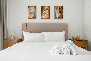 Quarto de hotel com cama, mesa de cabeceira, tomada na parede e três quadros acima da cama.