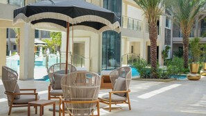 A poolside area with wicker chairs and a table, a large umbrella, and a palm tree. - 1BR Retreat | Pool & Jacuzzi | Near Eagle Beach (Noord)
