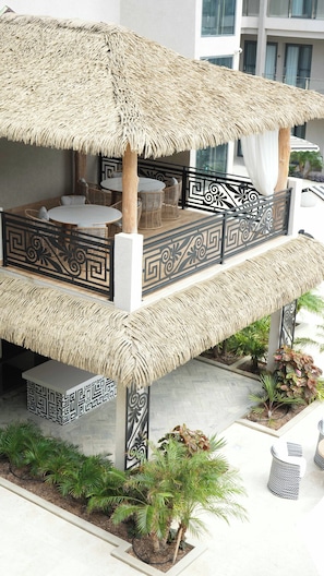 Un espace extérieur aménagé avec une toiture de chaume et une balustrade décorative, entouré de plantes en pot.