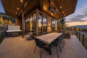 Une terrasse extérieure moderne, dotée d’une table et de chaises en bois, d’un barbecue et d’un bain à remous.