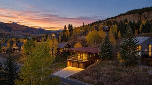 Une maison moderne dotée d’une grande terrasse, entourée d’arbres et offrant une vue sur les montagnes.