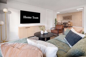 Ein modernes Wohnzimmer mit einer Couch, einem Couchtisch und einem Fernseher, der 'Home Team' zeigt.