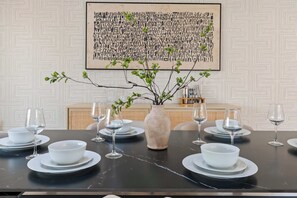 A dining table set with white plates and glasses, a vase with green branches, and a geometric patterned wall in the background. - Lakin' It Easy | Luxe Waterfront Oasis | Sleeps 16 (Mesa)