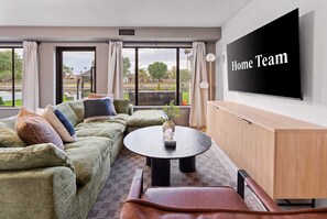 A modern living room with a sectional sofa, a round coffee table, and a flat-screen TV on the wall. - Lakin' It Easy | Luxe Waterfront Oasis | Sleeps 16 (Mesa)