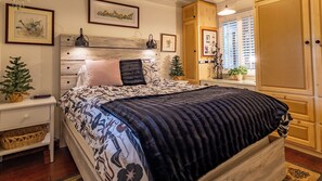 Ein Schlafzimmer mit einem Bett, Nachttischen, einem Schminktisch, einer Kommode, einem Fenster mit Jalousien und Wandbildern.