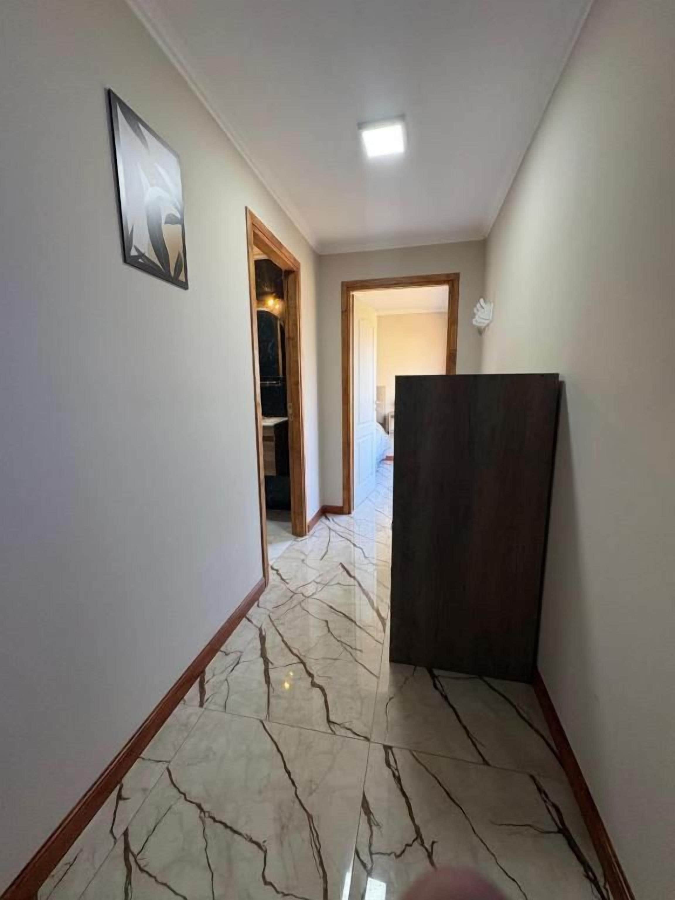 A hallway with a marble floor, a framed picture on the wall, and a door leading to another room.