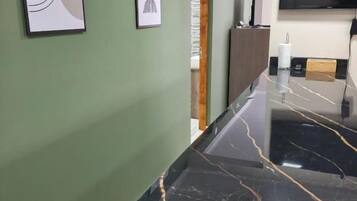 Una cocina con encimera de mármol negro, un televisor de pantalla plana montado sobre la encimera y cuadros en la pared.