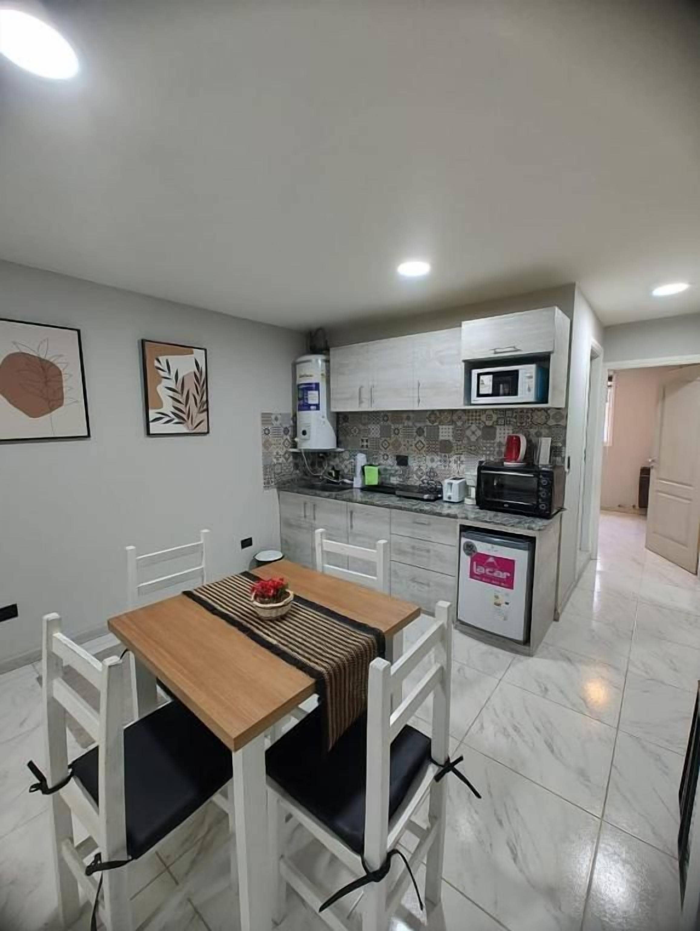 Una cocina compacta con armarios blancos, microondas y cafetera. Hay una mesa de comedor con sillas y una pequeña alfombra.