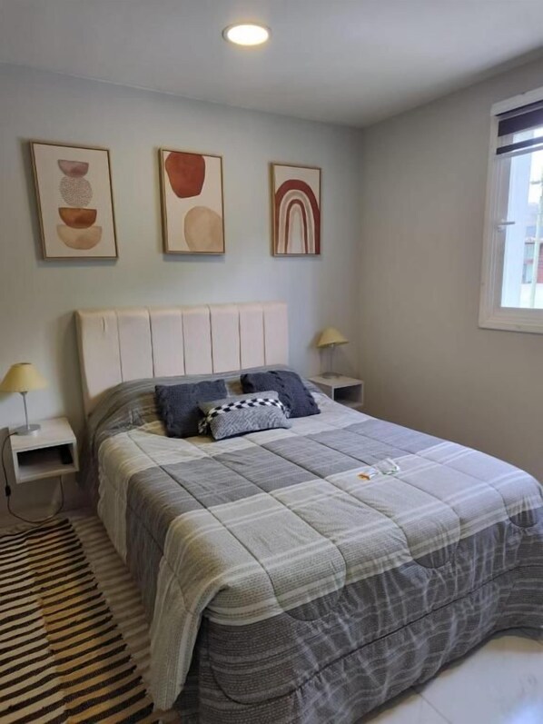 Un dormitorio con cama, mesitas de noche, una ventana y decoración en la pared.