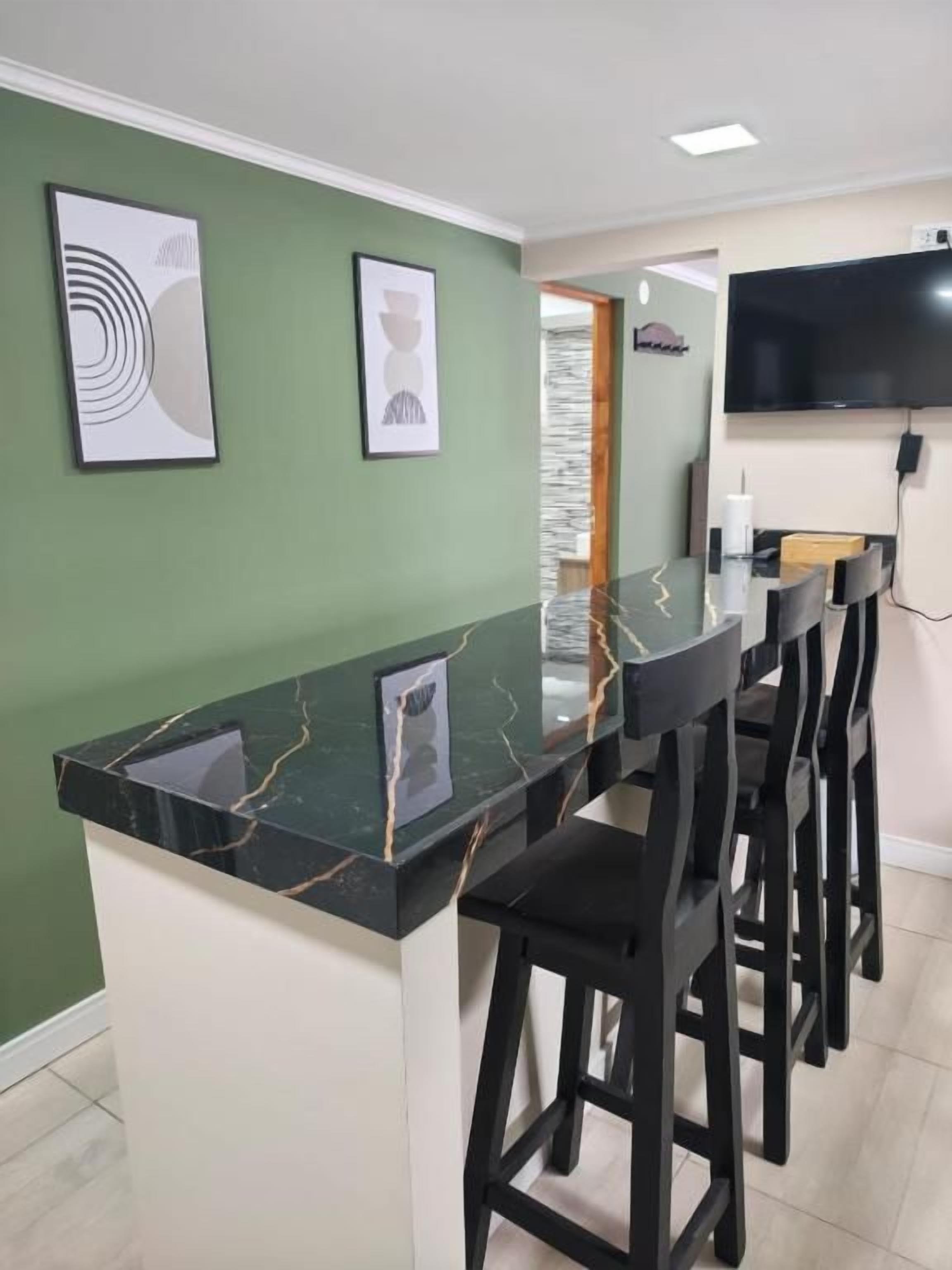 A bar area with a marble countertop, black bar stools, and a flat-screen TV mounted on the wall.