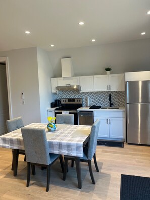 A modern kitchen with white cabinets, a stainless steel refrigerator, and a dining area with a table and chairs. - Charming York Sanctuary with Private Rooftop Oasis (Toronto)
