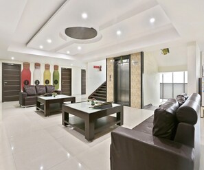A modern living room with a sofa, coffee table, and a staircase leading to an elevator. - Classic Halcyon Deccan Inn (Hyderabad)