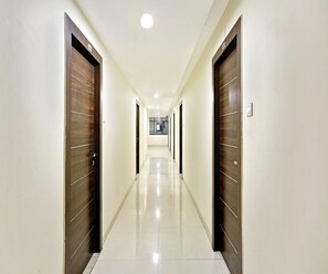 A hotel corridor with wooden doors, white walls, and a tiled floor. - Classic Halcyon Deccan Inn (Hyderabad)