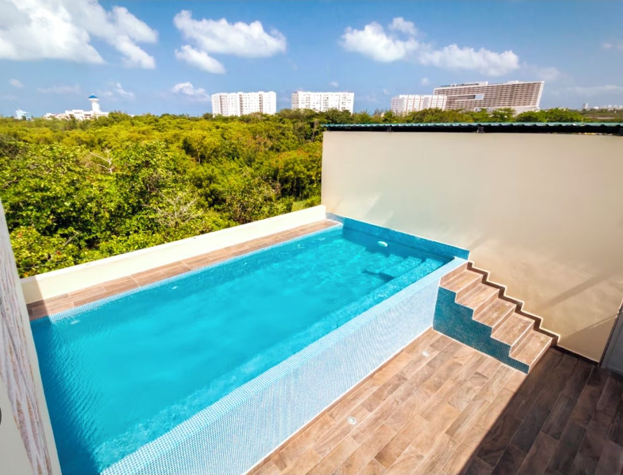 A swimming pool with a wooden deck and a view of a cityscape in the background.