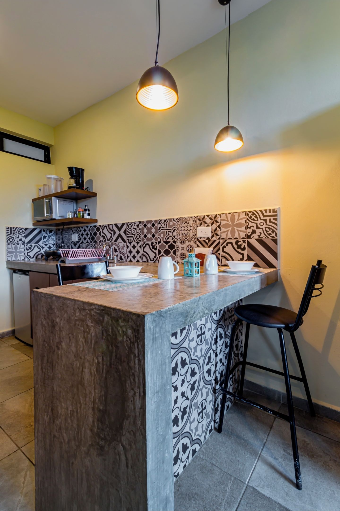 A kitchen with a central island, bar stools, a coffee machine, and patterned backsplash.