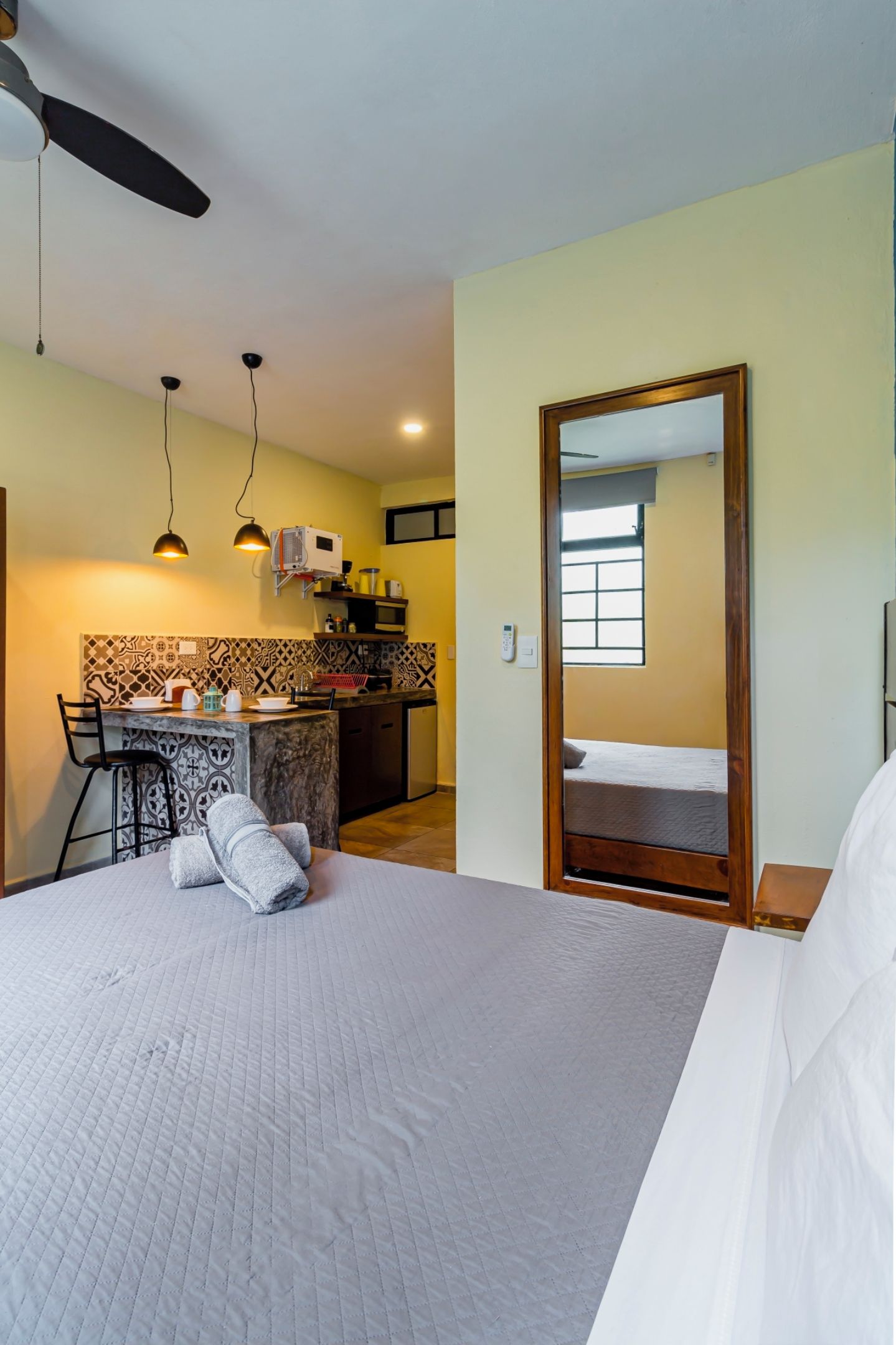 A hotel room with a bed, a desk with a chair, a kitchen area, and a bathroom.