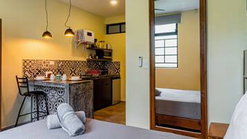 A hotel room with a bed, a desk with a chair, a kitchen area, and a bathroom.
