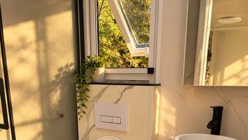 A modern bathroom with a toilet, sink, and a window with a plant.