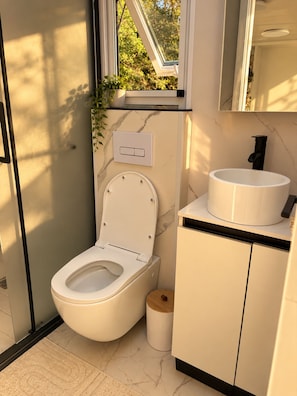 Et moderne badeværelse med toilet, håndvask og et vindue med en plante.