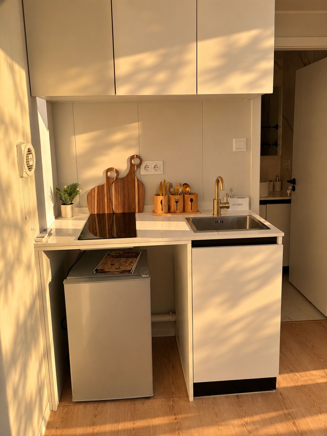 Une cuisine compacte dotée d’un évier encastré, d’un petit réfrigérateur et de planches à découper en bois.
