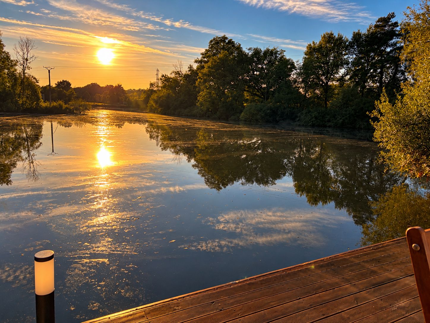 Une rivière paisible reflétant le coucher de soleil, avec une jetée en bois au premier plan.