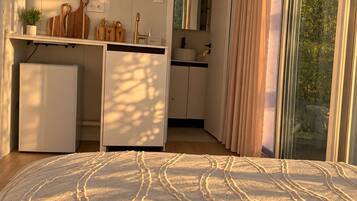 A bedroom with a bed, a kitchenette, and a sliding glass door to a balcony.