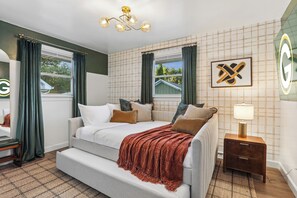 Ein Schlafzimmer mit Bett, Nachttisch, Lampe und einem Fenster mit Vorhängen.