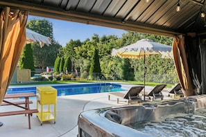Ein überdachter Außenbereich mit Whirlpool, Liegestühlen und Schwimmbecken.