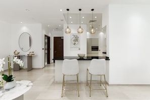Een moderne keuken met een centraal eiland, hanglampen en een eethoek met twee stoelen.