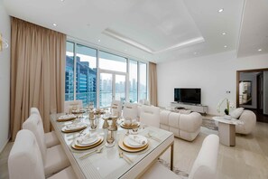 A modern living room with a dining area, large windows, and a flat-screen TV. - Refined 1BR Haven | Palm Jumeirah (Dubai)