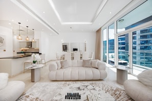 A modern living room with a sofa, a coffee table, and a dining area with chairs and a table. - Refined 1BR Haven | Palm Jumeirah (Dubai)